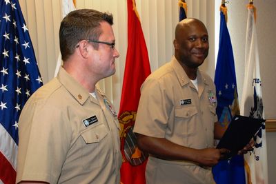 Two Navy officers in formal setting with flags displayed