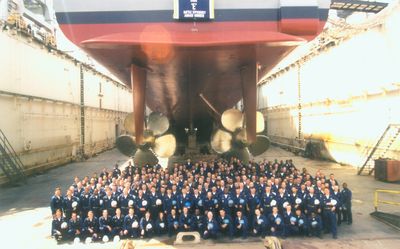 Large crew group photo in drydock with ship propeller visible