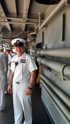 Below decks in dress whites, passageway lined with pipes and conduits