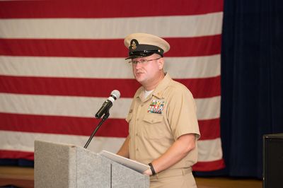 Speaking to the command from the podium, flag backdrop