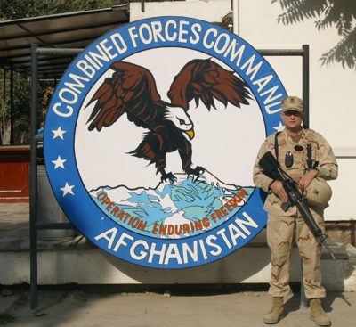 Sailor standing before the Combined Forces Command Afghanistan emblem